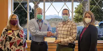 Four people standing by a window with two men exchanging a check