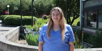 Young woman in scrubs standing in front of garden