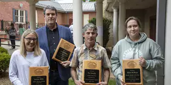 Four people holding plaques standing outside