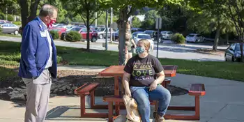 John Gossett standing in front of a student at a picnic table with dog sitting at student's feet. 