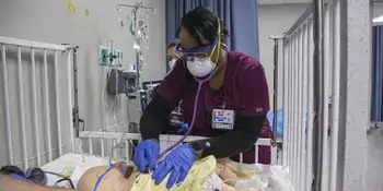 Nursing student in scrubs with stethoscope listening to simulated patient