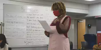 Young woman in mask standing reading a paper in a classroom