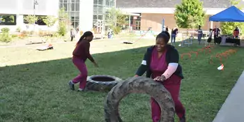 Two students in scrubs rolling tires on grass
