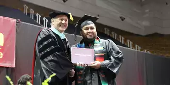 Dr. Gossett handing a diploma to male student at commencement