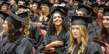 Student smiling while seated in her cap and gown at graduation