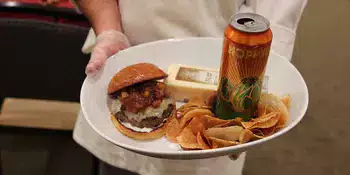 Chef holding white plate with hamburger and chips