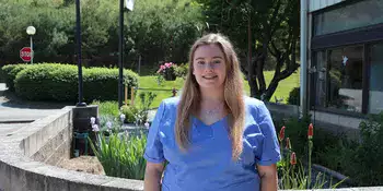 Young woman in scrubs standing in front of garden