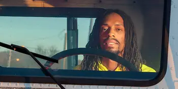 Man wearing yellow shirt sitting in the cab of a truck