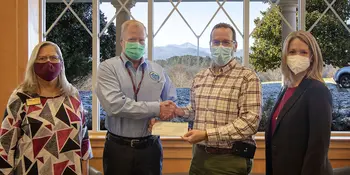 Four people standing by a window with two men exchanging a check