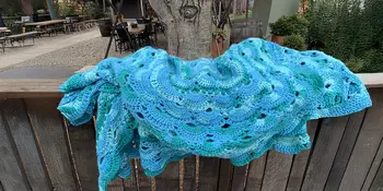 Crocheted green and blue blanket on a fence. 