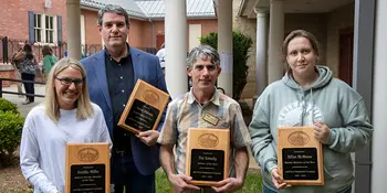 Four people holding plaques standing outside