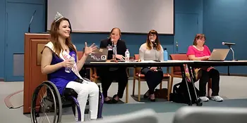 Madeline Delp in a wheelchair in front of three women at a table. 