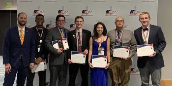 Seven well dressed chefs standing in front of a wall holding certficates