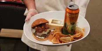 Chef holding white plate with hamburger and chips