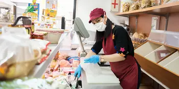 Woman behind food counter wearing gloves and mask
