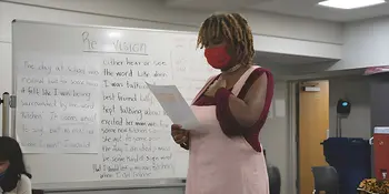 Young woman in mask standing reading a paper in a classroom